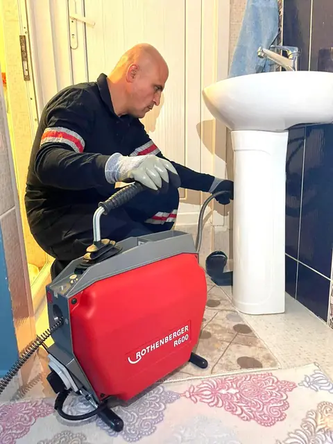 Banyo lavabosunun altından sökülen şişe sifon haznesi bir kovanın üzerinde temizleniyor.