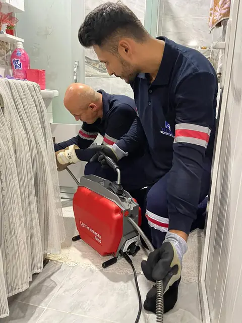 Teknisyen kireç tutmuş bir klozetin çıkış borusuna kamera sürerek içini görüntülüyor.